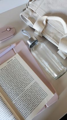 an open book with a water bottle next to it on top of a white table