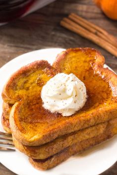 two pieces of french toast on a white plate with whipped cream and cinnamon sticks next to it