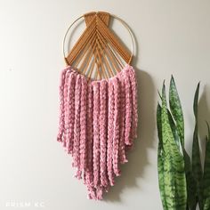 a pink crocheted wall hanging next to a potted plant