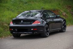 a black sports car is parked on the side of the road in front of some grass