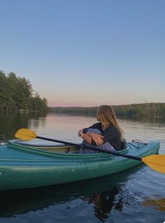 a woman sitting in a green kayak on the water with trees and sky behind her