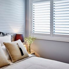 a bed with white sheets and pillows in front of a window that has blinds on it