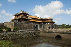 an old chinese building with water in the foreground and clouds in the sky above