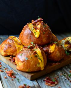 a wooden board topped with cheesy bread muffins covered in cheese and bacon