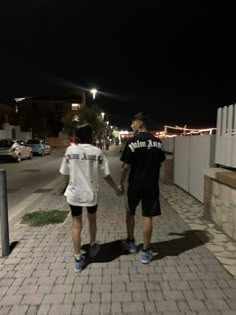 two young men walking down the street at night with their hands in each other's pockets