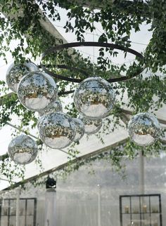 several clear glass balls hanging from the ceiling in an outdoor area with greenery and white walls