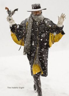 a man in a hat and coat is walking through the snow with his hands up