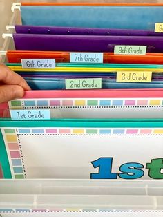 a person holding a stack of colorful folders with the number one on them and labeled 1st grade