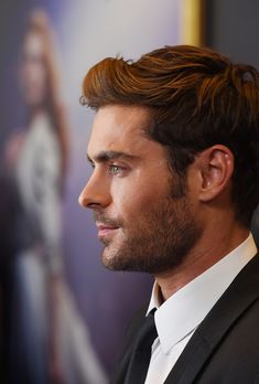 a close up of a person wearing a suit and tie with a poster in the background