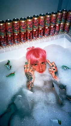 a woman with pink hair sitting in a bathtub filled with lots of booze