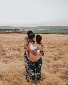 a pregnant woman hugging her husband while standing in the middle of a field at sunset