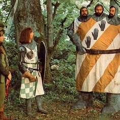 several people dressed in medieval costumes standing around a giant statue with hands on it's chest