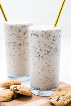 two glasses filled with cookies and milk sitting on top of a cutting board