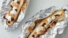 two sandwiches wrapped in tinfoil with toppings on them sitting next to each other