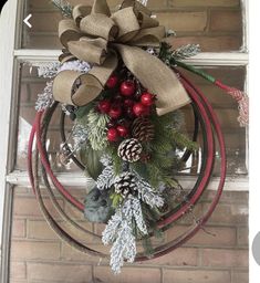 a wreath hanging on the front door with pine cones, berries and evergreens attached to it