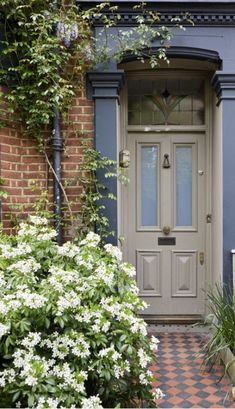 the front door of a house with blue shutters and white flowers on either side