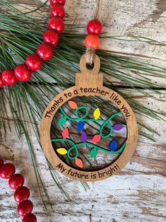 a wooden ornament hanging from a pine tree with christmas lights on it and the words, there is a teacher like me in my future is bright