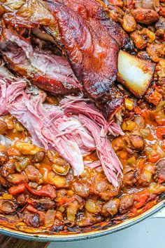 meat and beans cooking in a pot on top of a wooden table with utensils