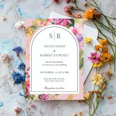 the floral wedding stationery is laid out on top of marble with flowers surrounding it