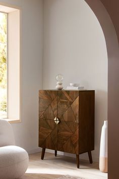 a living room with a white chair and a wooden cabinet in front of a window