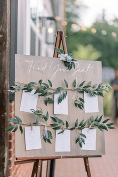 an easel with seating cards and greenery on it