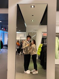 two people standing in front of a mirror taking a selfie with their cell phones