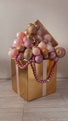 a gold gift bag with balloons in it on the floor next to a white wall