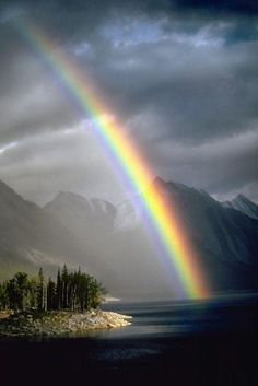 a rainbow shines brightly in the sky over a lake and mountain range on a cloudy day