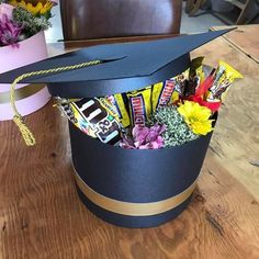 a graduation cap with candy bars and flowers in it on a table next to a pink box