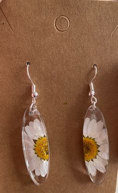 two clear glass earrings with yellow and white flowers on them sitting on a piece of cardboard