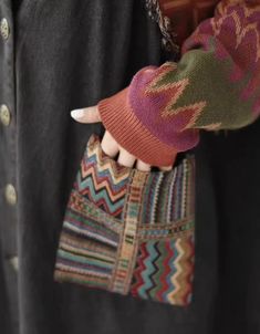 a woman's hand holding a multicolored purse on her left wrist and right arm