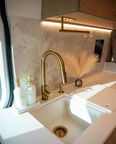 a white sink with gold faucet and soap dispenser