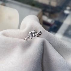 a diamond ring sitting on top of a white cloth in front of a cityscape