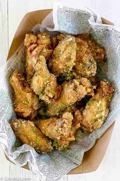 fried chicken wings in a basket on top of a white wooden table with napkins