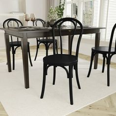 a dining room table with four chairs and a rug on the floor in front of it