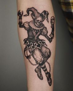 a black and white tattoo of a clown with chains on his legs, holding a skull