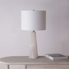 a table with a lamp on it next to a book and a white wall in the background