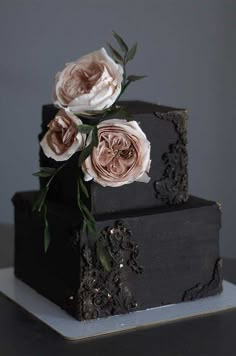 a three tiered black cake with flowers on the top and bottom, sitting on a white plate