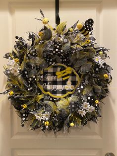 a yellow and black wreath hanging on the front door with monogrammed letters surrounded by flowers