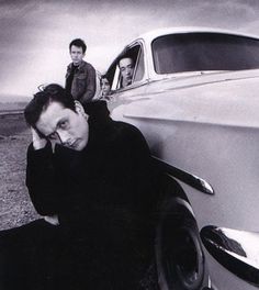 two men sitting on the ground next to an old car and one is holding his head