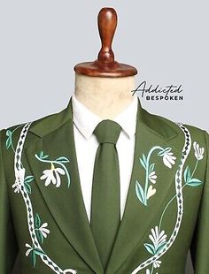 a green suit with white flowers and chains on the lapel is displayed in front of a mannequin