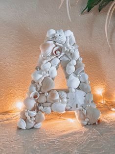 a decorative letter made out of seashells sits on a table next to some lights