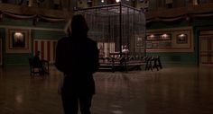 a woman is standing in the middle of a room with a birdcage hanging from it's ceiling