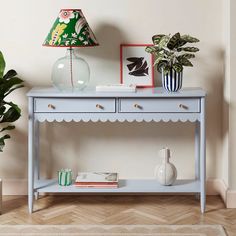 a blue table with two drawers and a lamp on it next to a potted plant