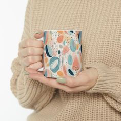 a woman holding a coffee mug in her hands while wearing a beige sweater and green nail polish