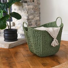 a green basket sitting on top of a wooden floor next to a potted plant