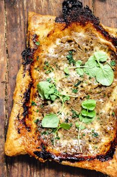 a square piece of pizza with cheese and herbs on it sitting on a wooden surface