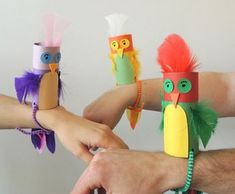 four people holding up colorful paper owls with feathers on them'heads and hands in the air