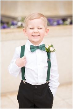 a young boy in a white shirt and green suspenders smiles at the camera while wearing a bow tie