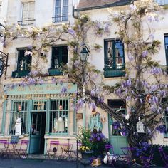 an old building with purple flowers growing on it's side and windows in the front